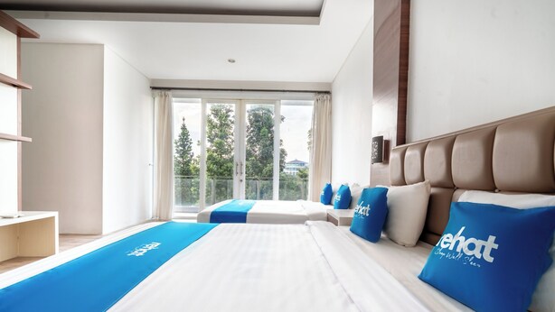 A modern hotel room with a large bed, a view of trees through the window, and a balcony. - Rehat at Villa Golf Island Dago Resort I (Cimenyan)