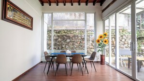 A dining area with a table and chairs, a stone wall outside, and a large window with a view of the outdoors. - Rehat at Villa Golf Island Dago Resort I (Cimenyan)