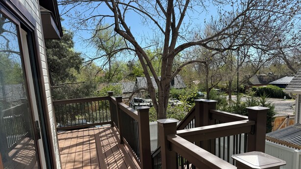 Una terraza de madera con barandilla, un árbol y vista a una zona residencial.