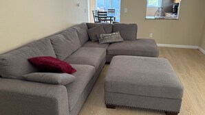 Un salón con un sofá seccional gris, una almohada roja y un reposapiés a juego.