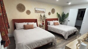 Une chambre d’hôtel avec deux lits, un plancher en bois, une petite table, une plante et un tableau au mur.