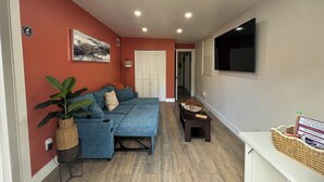 Un salon moderne avec un canapé d’angle, un téléviseur à écran plat et une petite table sur laquelle se trouve un panier.