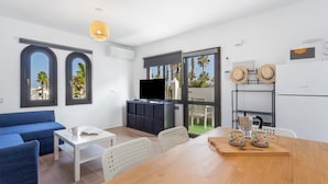 A modern living room with a blue sofa, a white coffee table, a TV, and a dining area with a wooden table and chairs. - Vacation Apartment 'Brisa Azul' with Shared Pool, Private Terrace and Wi-Fi (Corralejo)