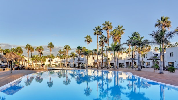 A swimming pool surrounded by palm trees and white buildings. - Vacation Apartment 'Brisa Azul' with Shared Pool, Private Terrace and Wi-Fi (Corralejo)