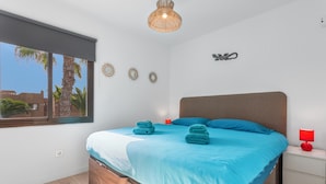A bedroom with a bed, a window, a bedside table, and a wall decoration. - Vacation Apartment 'Brisa Azul' with Shared Pool, Private Terrace and Wi-Fi (Corralejo)