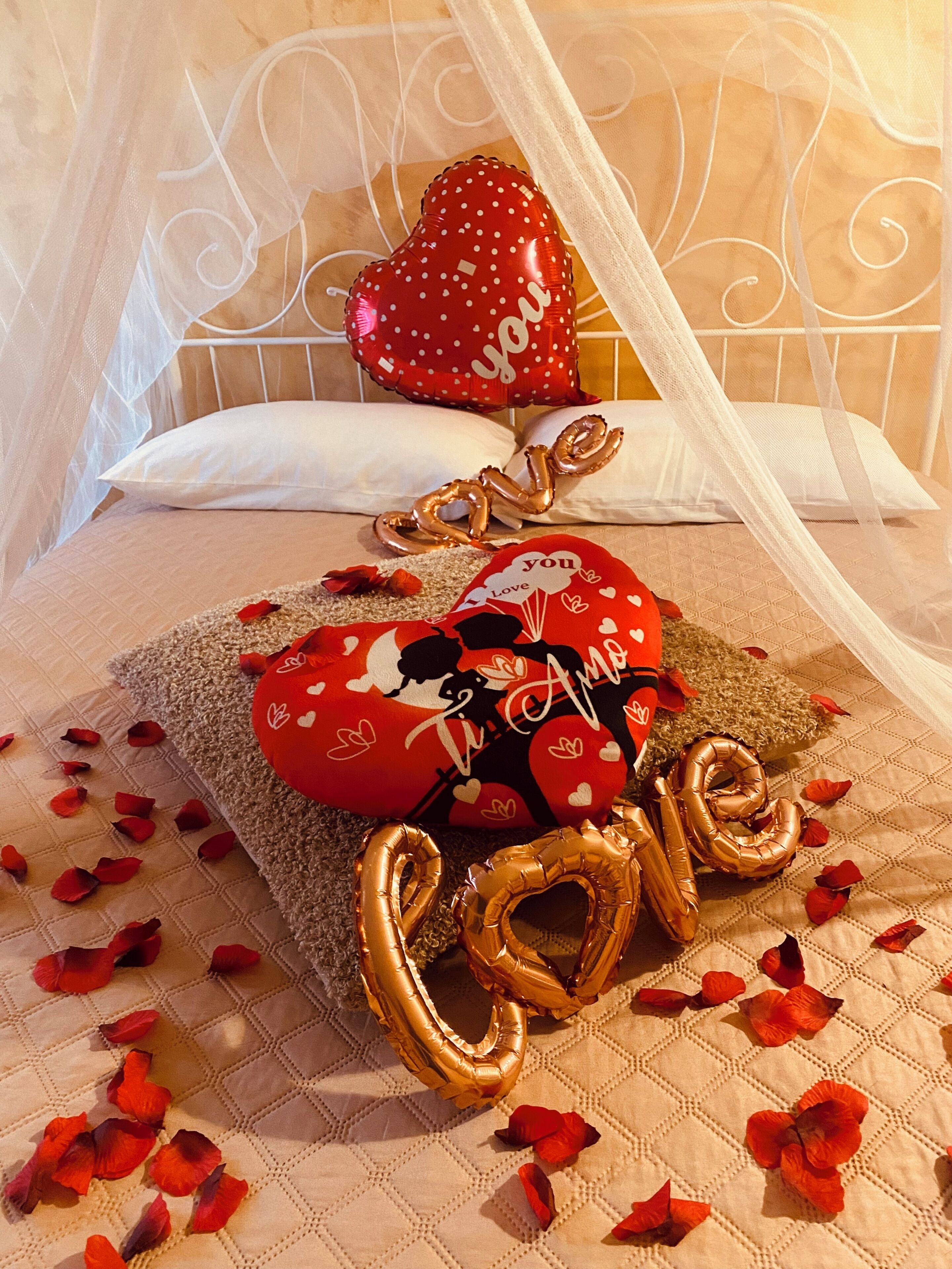 Un letto a baldacchino, con un cuscino a forma di cuore e un cuscino con la scritta 'Ti amo'.