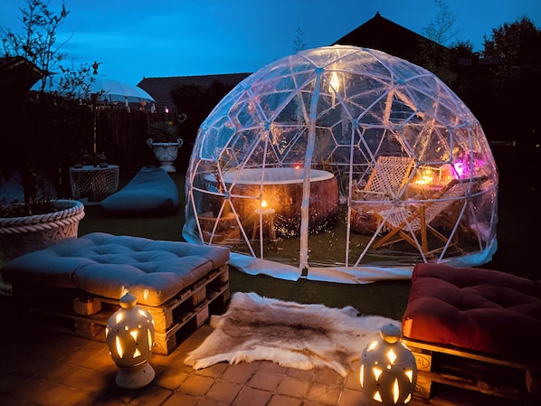 A geodesic dome structure with a fire pit inside, surrounded by outdoor furniture and lanterns.