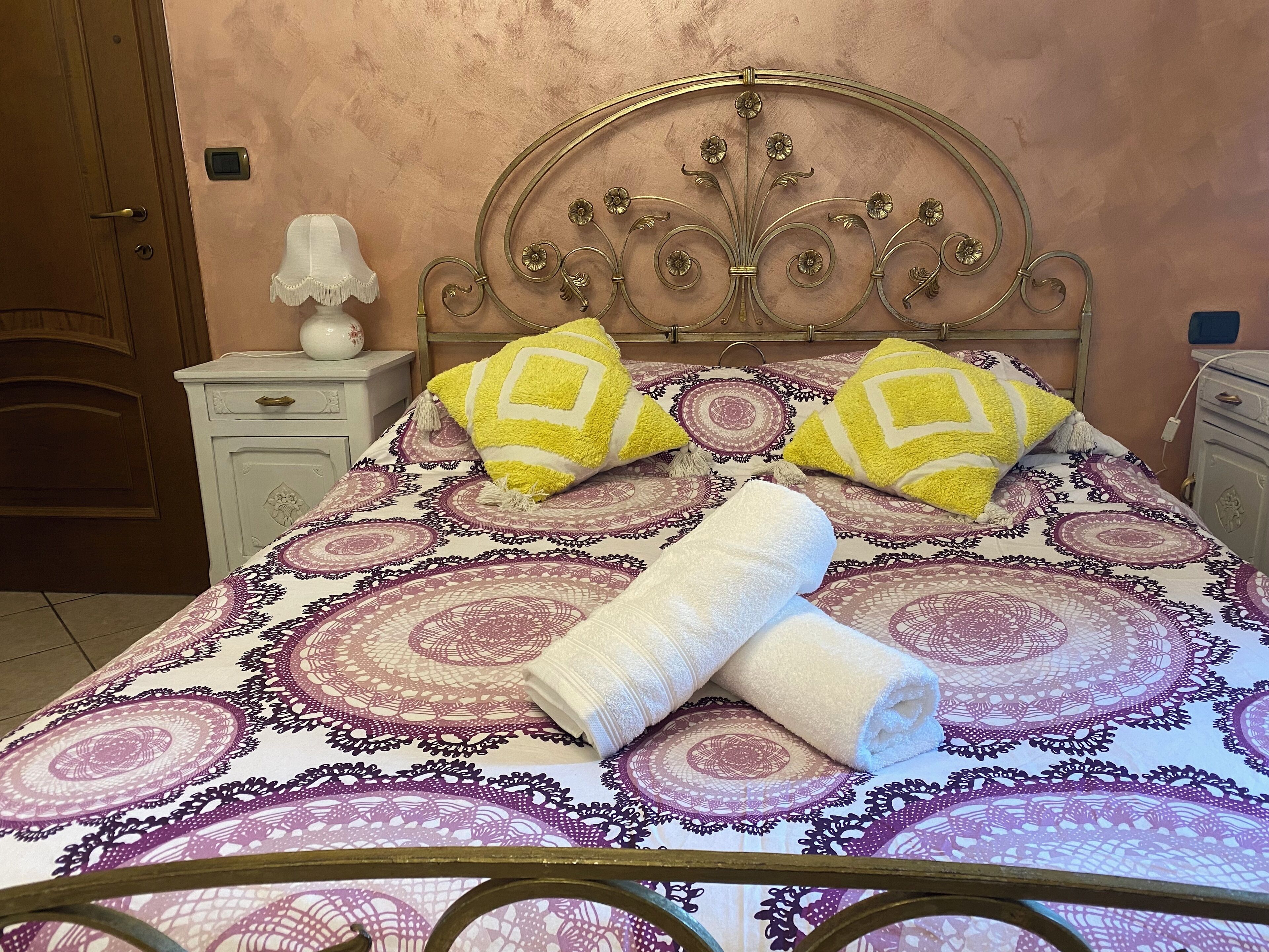 A bed with a patterned bedspread, two pillows, and two rolled towels.