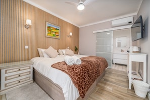 Quarto com cama, mesa de cabeceira, cômoda, televisão e um quadro na parede.