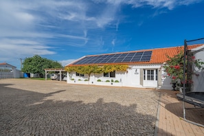Um edifício com telhado telhado, painéis solares e um pátio pavimentado.