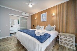 Une chambre à coucher comprenant un lit, des tables de chevet, un ventilateur de plafond, un climatiseur mural et une grande fenêtre.