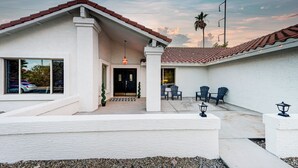 A house with a white exterior, a tiled roof, and a covered patio area with chairs and a table.