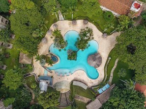 An aerial view of a resort with a central swimming pool, surrounded by lush greenery and palm trees. - Matapalo 202-Poolside Condo at Tamarindo (Tamarindo)