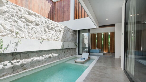 Un espace piscine extérieur moderne, agrémenté d’un mur en pierre, d’une chaise longue et d’une porte vitrée donnant sur une terrasse en bois.
