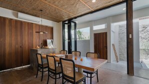 Un espace de repas moderne avec une table et des chaises en bois, un luminaire suspendu et une vue sur l’extérieur.