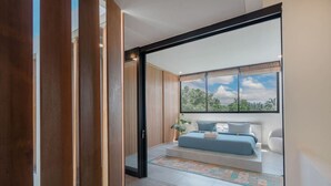 Une chambre moderne avec une grande fenêtre, un lit avec une literie bleue et une vue sur la verdure à l’extérieur.