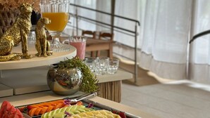 A buffet with a variety of fruits, cheeses, and meats. There are also decorative items like golden statues and a glass container with a golden liquid. - Oasis do Mar Hotel (Itapema)