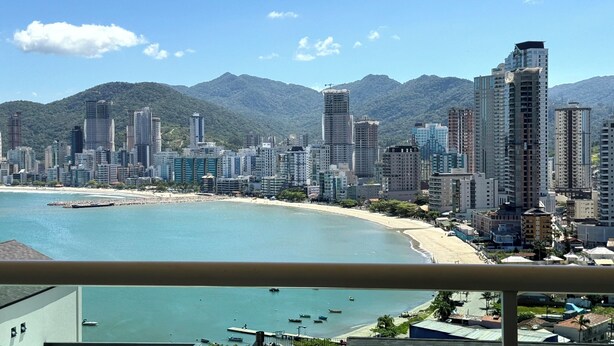 A coastal cityscape with high-rise buildings, a beach, and mountains in the background. - Oasis do Mar Hotel (Itapema)