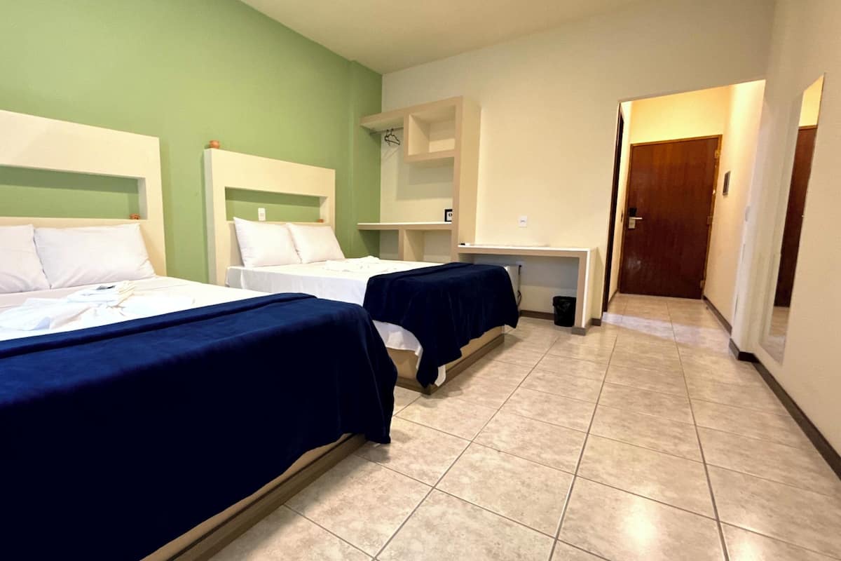 Quarto de hotel com duas camas, uma mesa de trabalho e um banheiro pequeno.