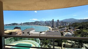 A balcony with a view of a coastal cityscape, including a beach and a city skyline with high-rise buildings. - Oasis do Mar Hotel (Itapema)