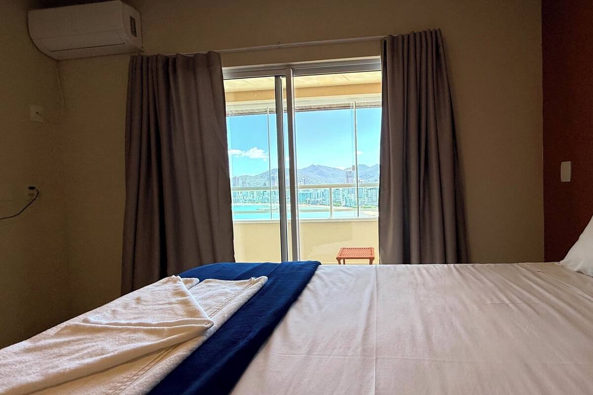 Quarto de hotel com uma cama, janela com cortinas e vista para a cidade.