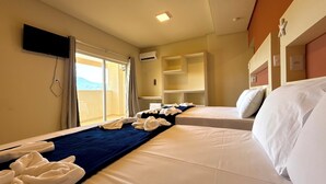A hotel room with two beds, a TV mounted on the wall, and a sliding glass door leading to a balcony. - Oasis do Mar Hotel (Itapema)