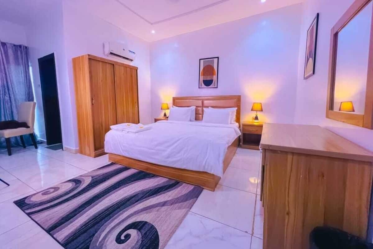 A hotel room with a bed, bedside lamps, a desk, a wardrobe, and a mirror.