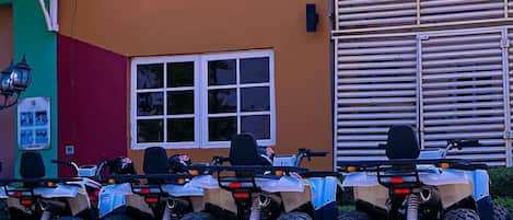 A row of quad bikes parked in front of a building with a window and a door.