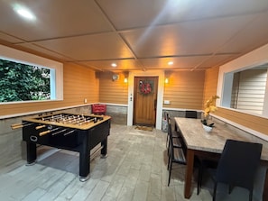 A room with a foosball table, a dining area with chairs and a table, and a door with a wreath.