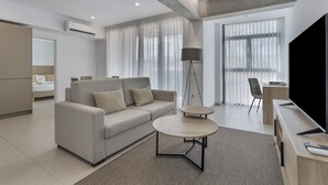 Ein modernes Wohnzimmer mit einer Couch, zwei Beistelltischen, einer Stehlampe, einem Fernseher und einem Essbereich mit Stuhl und Tisch.