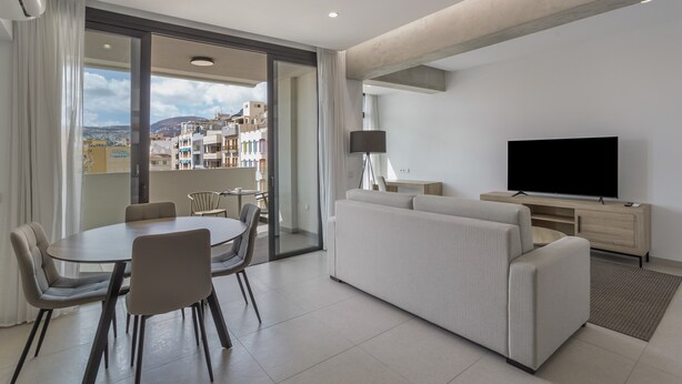 Ein modernes Wohnzimmer mit Essbereich, einer Couch, einem Fernseher und einem Balkon mit Blick auf die Stadt.