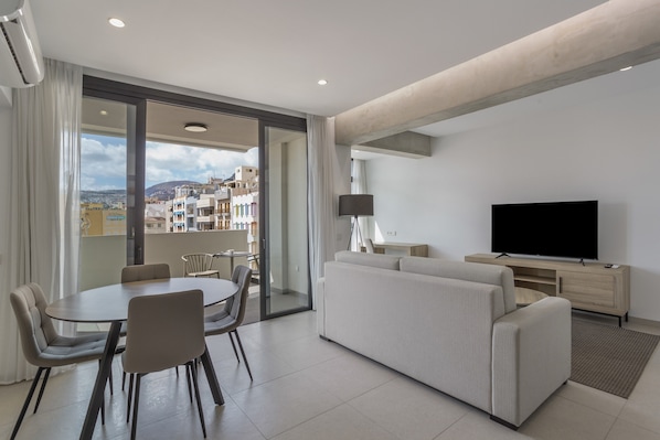 A modern living room with a dining area, a sofa, a TV, and a balcony with a city view.