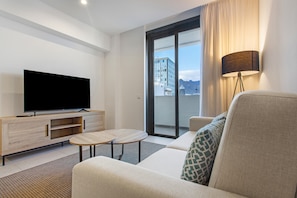 A modern hotel room with a flat-screen TV, a sofa, a small table, and a view of a building through a large window.