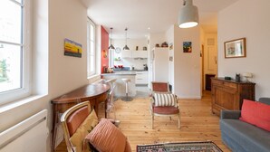 A modern apartment with a wooden floor, a dining area with a wooden table and chairs, a kitchen with white cabinets, and a living area with a sofa and a red cushion. - Bright and quiet apartment in the heart of Lyon (Lyon)
