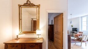 A wooden dresser with a large ornate mirror and two lamps, a wooden door, and a seating area with a chair and a small table. - Bright and quiet apartment in the heart of Lyon (Lyon)