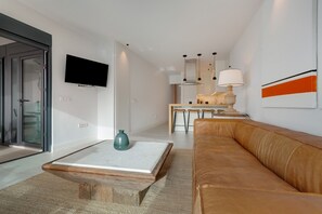 A modern living room with a sofa, a coffee table, a TV, and a dining area with chairs.