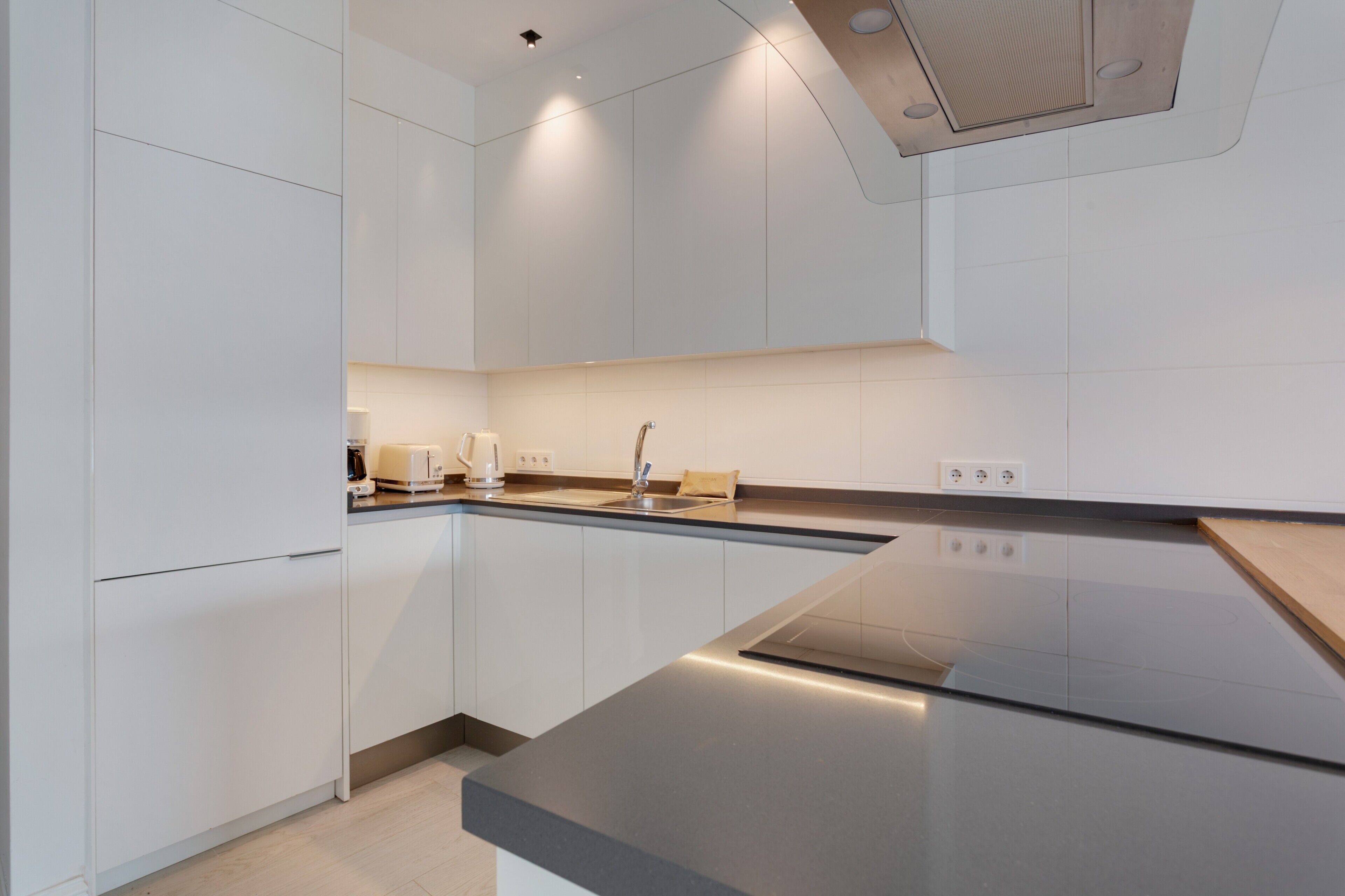 Une cuisine moderne avec des meubles blancs, un plan de travail en acier inoxydable et un four encastré.