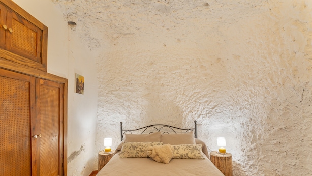 Une chambre avec un plafond en pierre rustique, une armoire en bois, un lit avec deux tables de chevet et une petite table de nuit avec une lampe.