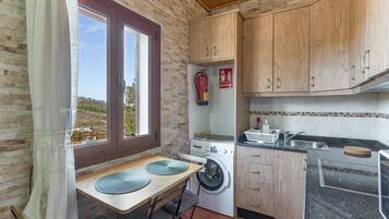 Eine kompakte Küche mit Waschmaschine, Holzschränken, einem Spülbecken und einem Fenster mit Blick auf eine hügelige Landschaft.