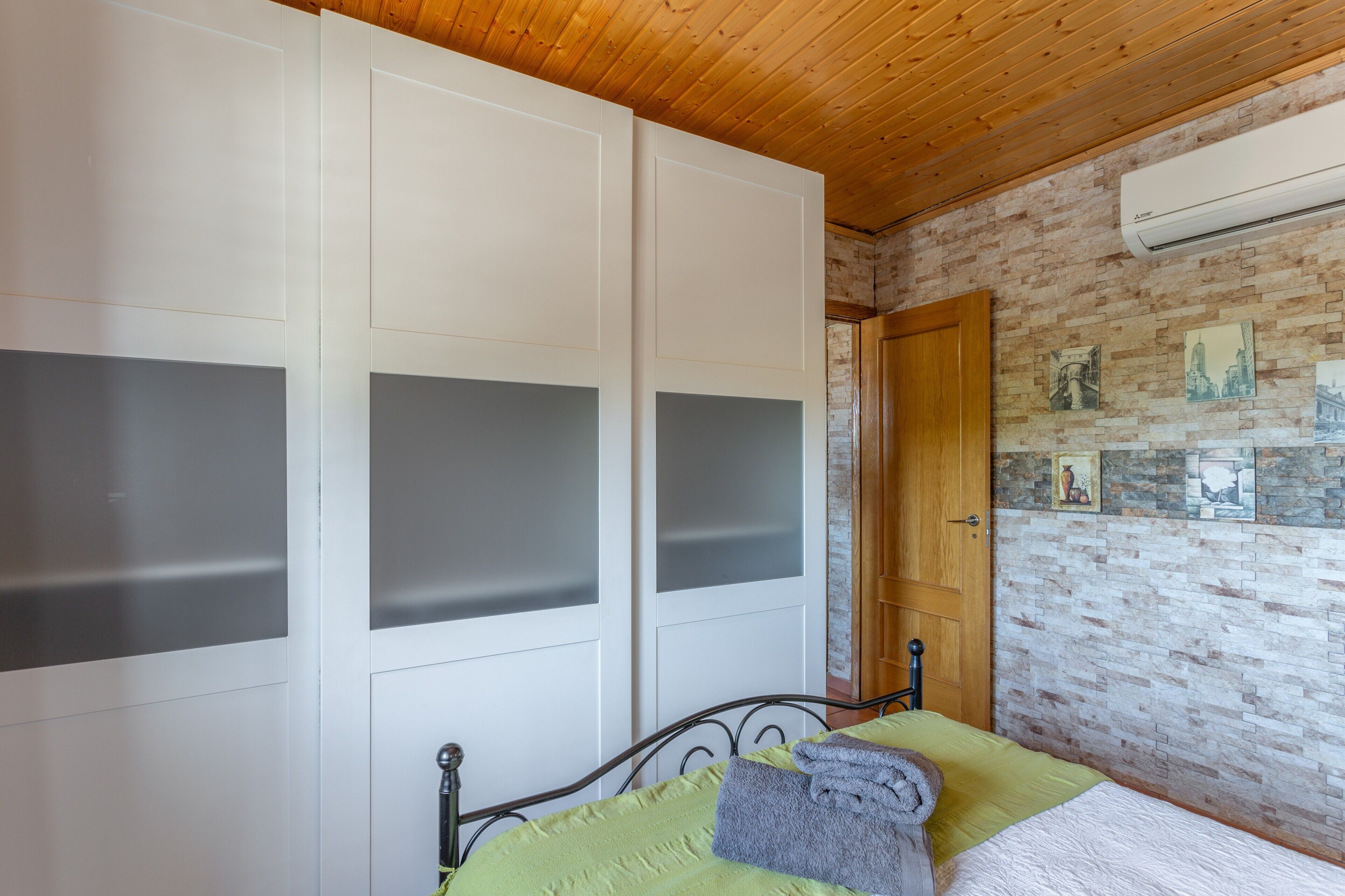 Un dormitorio con una cama, una puerta de madera, un muro de ladrillo y un equipo de aire acondicionado.