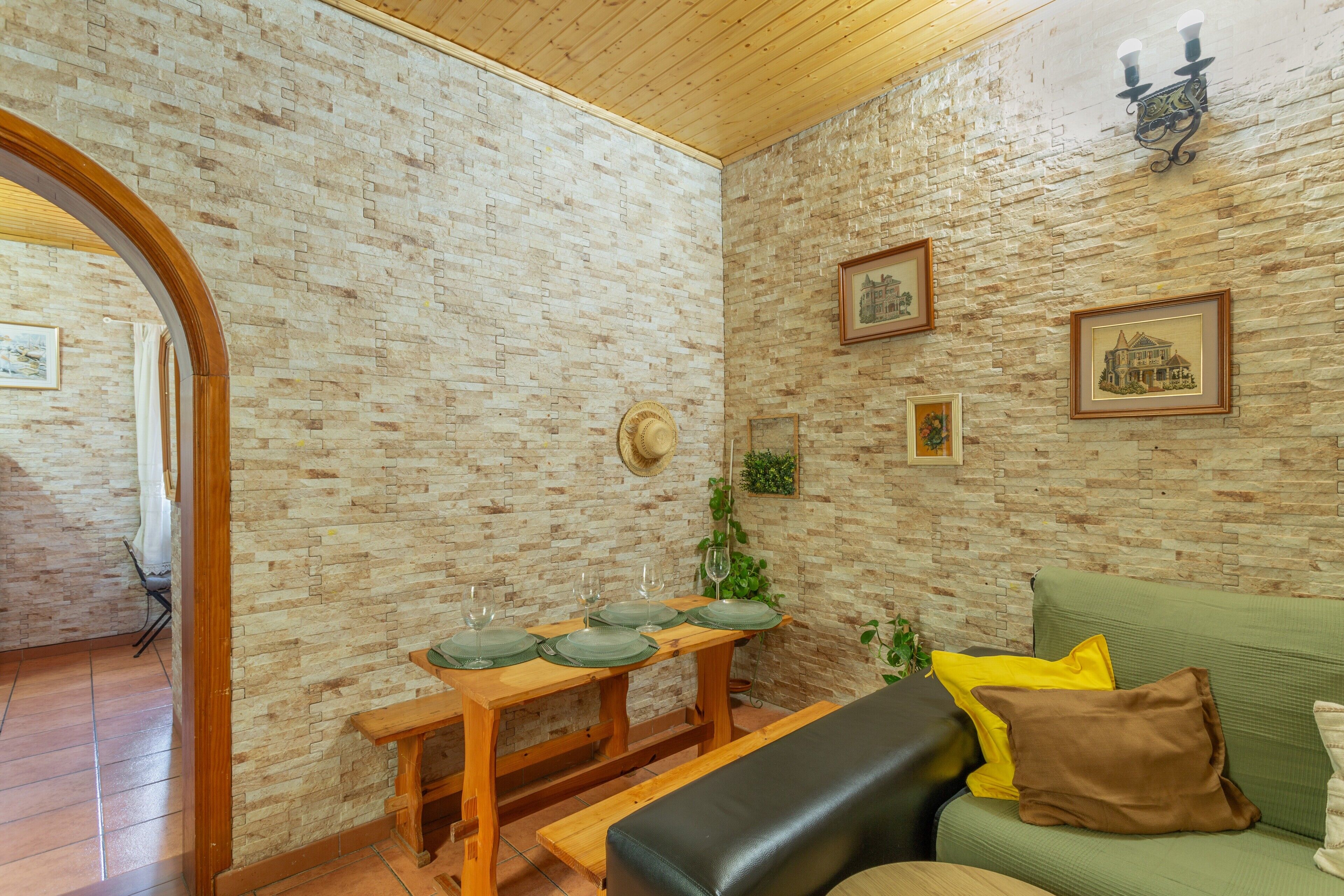Habitació amb paret de maó, sostre de fusta, un sofà verd, taula de fusta amb plats verds, i quadres emmarcados.