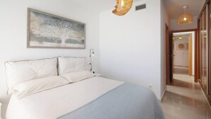 A bedroom with a large bed, a bedside table, a wall-mounted lamp, and a painting of a tree. - Relaxation, Golf and Beach (Velez-Malaga)