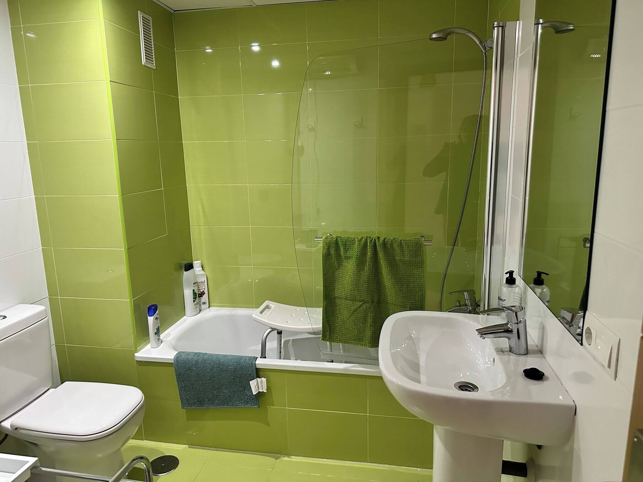 A bathroom with green tiles, a white sink, a bathtub, and a toilet.