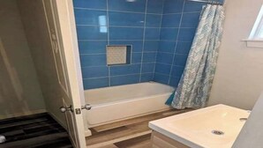 A bathroom with a bathtub, a shower curtain, and a sink.