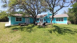 A two-story house with a large tree in front, a picnic table, and a covered outdoor seating area.