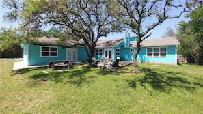A two-story house with a large tree in front, a picnic table, and a covered outdoor seating area. - 2 Large Bedrooms | Private | Downtown (Manchaca)
