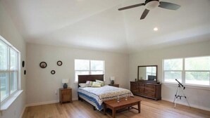 A spacious bedroom with a large bed, a desk, a dresser, and a ceiling fan.