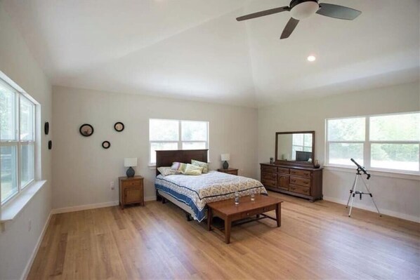 Un dormitorio amplio con una cama grande, un escritorio, un aparador y un ventilador de techo.