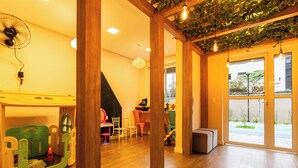 Een kamer met houten vloer, een speelruimte met kleurrijk speelgoed, een ventilator en uitzicht door grote ramen.