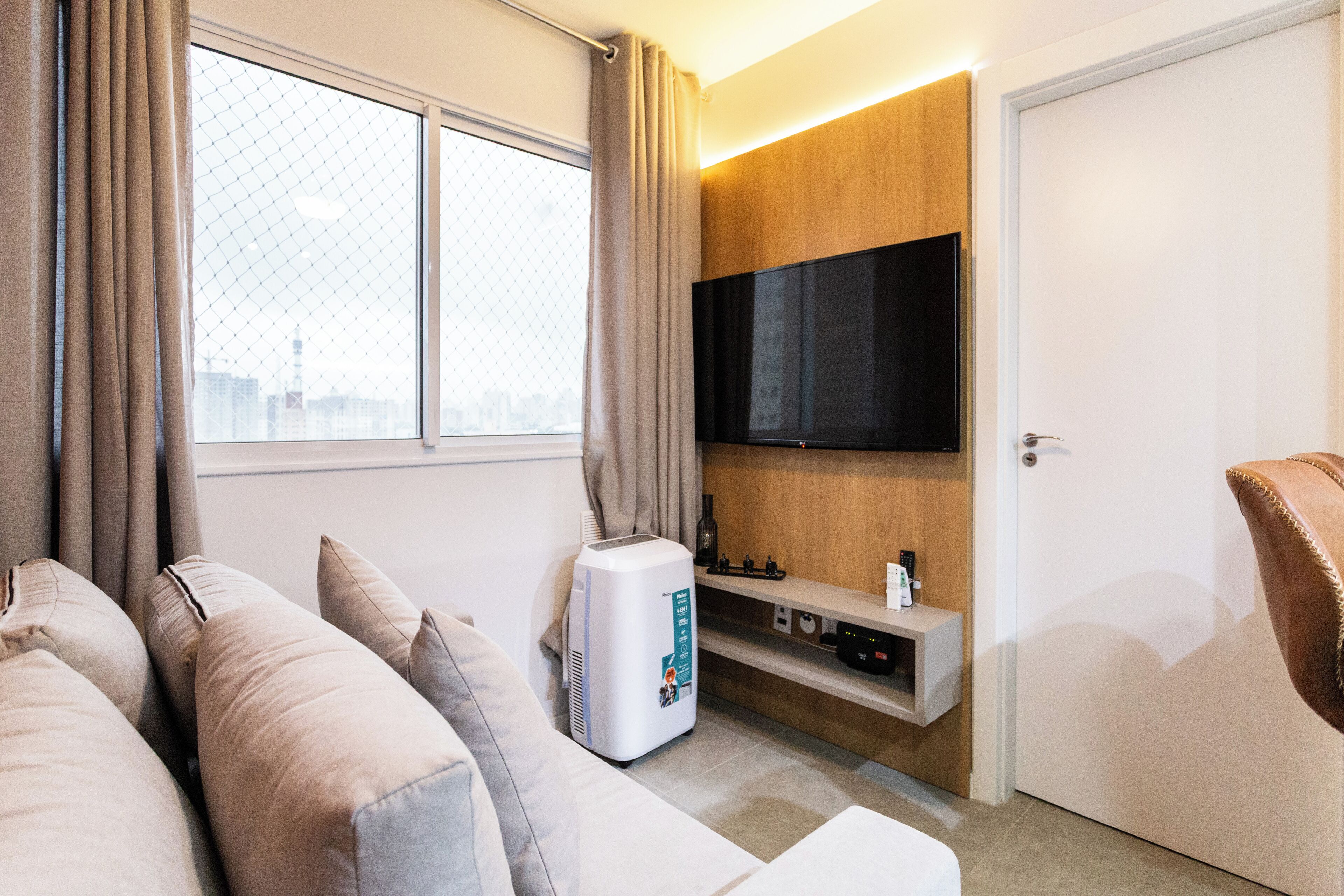 A modern living room with a sofa, a flat-screen TV mounted on the wall, a small table with a bottle, and a door.